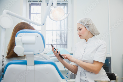 Female dentist and patient discussing treatments in a tablet application. Stomatologist showing patient her case on digital aplication