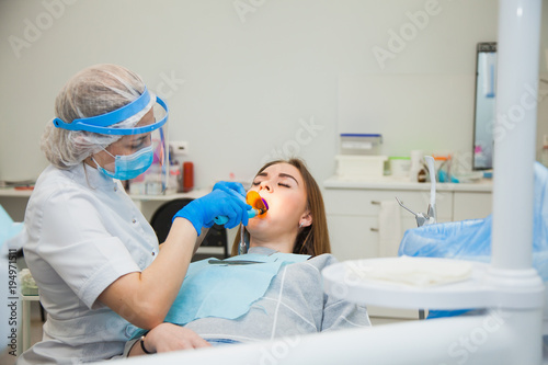 Female dentist work with light-curing seal  patient with caries on chair. Stomatologist and patient at clinical office. Toothcare concept