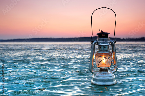 winter evening on frozen lake, vintage lantern at sunset