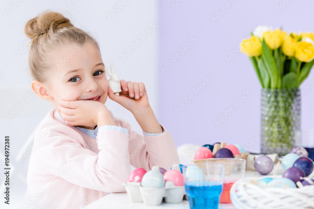 Little child playing with Easter bunny statuette and painted eggs Little child playing with Easter bunny statuette and painted eggs