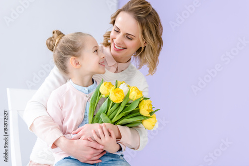 Cute child embracing mother with tulips bouquet on 8 march