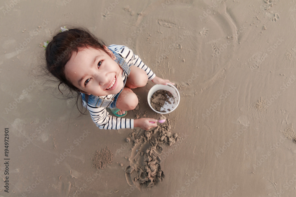 Naklejka premium Top view portriat Asian little girl playing on the sand beach with evening ambient