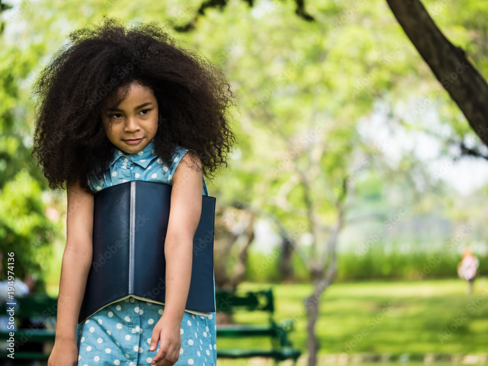 Beautiful girl holding a book, against green of summer park.