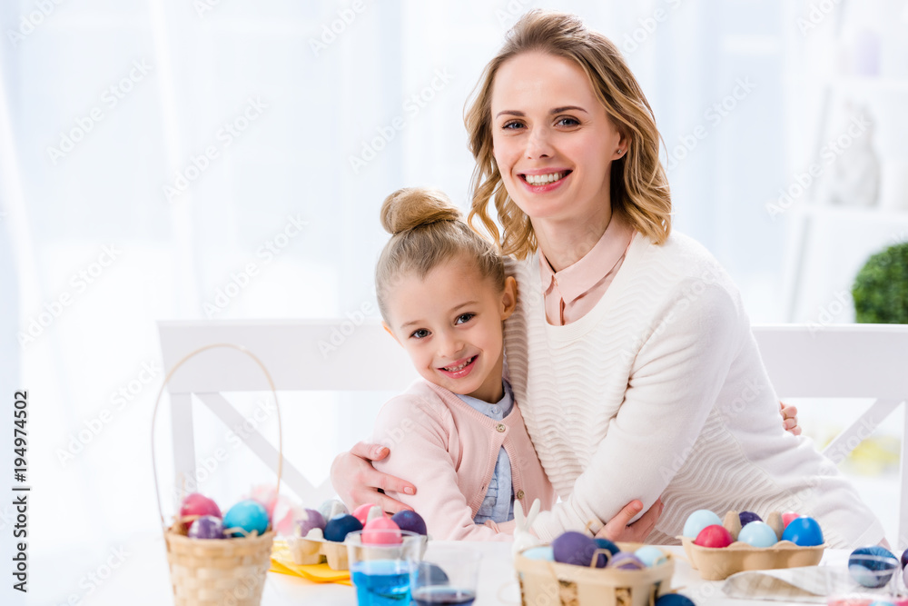 Fototapeta premium Mother and daughter embracing by table with painted Easter eggs