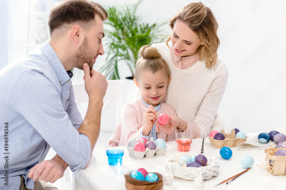 Parents and daughter painting Easter eggs in different colors Parents and daughter painting Easter eggs in different colors