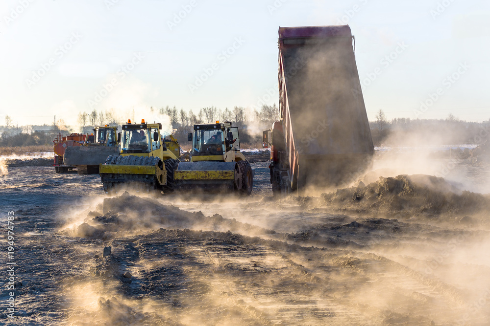 roller compacts soil in embankment on the road's construction. sand consolidation on road-building. Compactor driving on sandy. wheel marks on the sand. hard work. transportation of sand by trucks roller compacts soil in embankment on the road's construction. sand consolidation on road-building. Compactor driving on sandy. wheel marks on the sand. hard work. transportation of sand by trucks