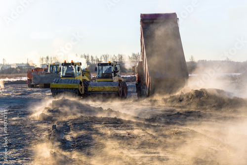 roller compacts soil in embankment on the road's construction. sand consolidation on road-building. Compactor driving on sandy. wheel marks on the sand. hard work. transportation of sand by trucks