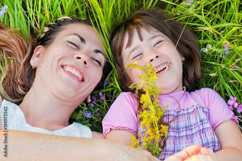 young, beautiful mother with little daughter, happy and laughing on a walk in the grass with flowers on a sunny, summer day. The concept of motherhood and a happy childhood