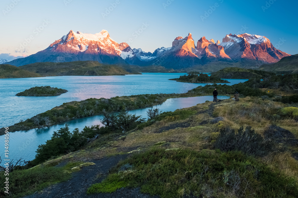 Torres del Paine National Park, lake of Pehoe with islets during sunrise. Two photographers are visible on top of the hill at right part of the frame