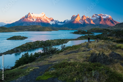 Fototapeta Naklejka Na Ścianę i Meble -  Torres del Paine National Park, lake of Pehoe with islets during sunrise. Two photographers are visible on top of the hill at right part of the frame
