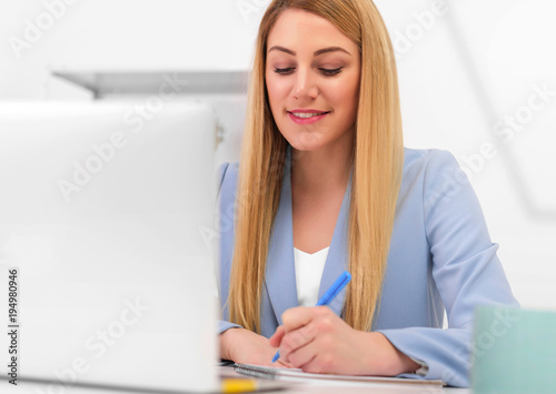 Attractive young woman working with documents and laptop in the workplace in a white office.