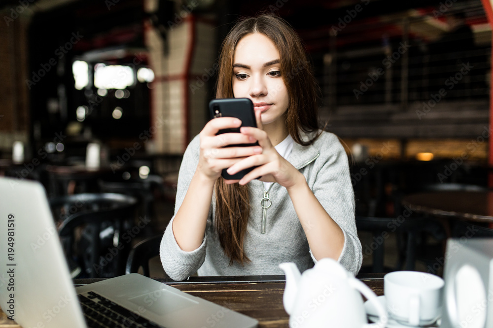 Young woman or successful working on smart phone and laptop computer at coffee shop interior. Girl student sitting in university cafeteria while using technology. Young woman or successful working on smart phone and laptop computer at coffee shop interior. Girl student sitting in university cafeteria while using technology.