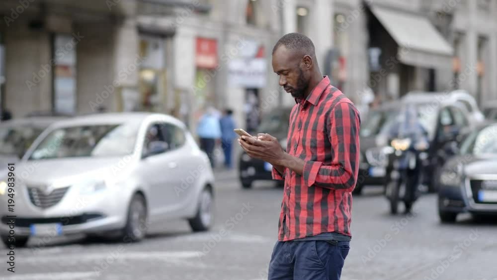 Portrait of young black man typing on smartphone in the street Portrait of young black man typing on smartphone in the street