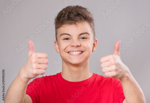 Close-up emotional portrait of caucasian teen boy wearing red t-shirt. Funny teenager making thumbs up gesture  isolated on white background. Handsome child laughing looking very happy.