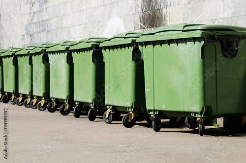 A row of green garbage containers on the city street.