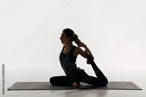 side view of woman practicing yoga and doing king pigeon on white