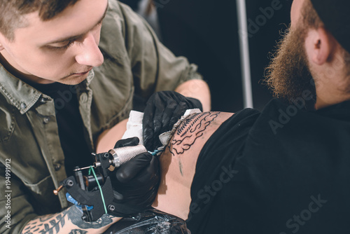 Tattoo artist and bearded man during tattooing process in studio