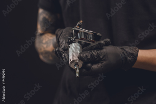 Male hands in gloves holding tattoo machine isolated on black photo