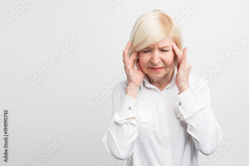 Sick and old woman is touching her head showing she has a headache. Probably she will get sick. Close up. Isolated on white background.