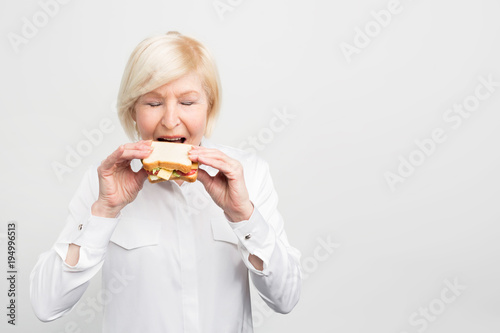 Mature and satisfied woman is eating her homemade sandwich with pleasure. She is ready to have a first bite of this meal. Isolated on white background. photo