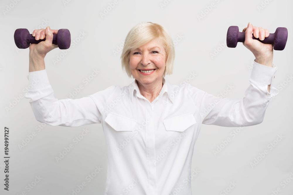 Cheerful madam is exercising with light weights. She does that because she has a careless retirement and much time to do that. Isolated on white background. Cheerful madam is exercising with light weights. She does that because she has a careless retirement and much time to do that. Isolated on white background.