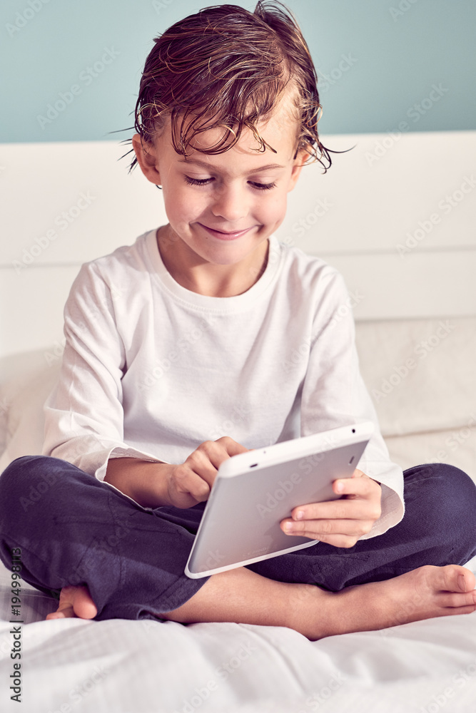 Smiling boy using a digital tablet while sitting on bed Smiling boy using a digital tablet while sitting on bed