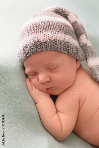 likable and pretty sleeping newborn baby girl with in a knitted hat on a blue background