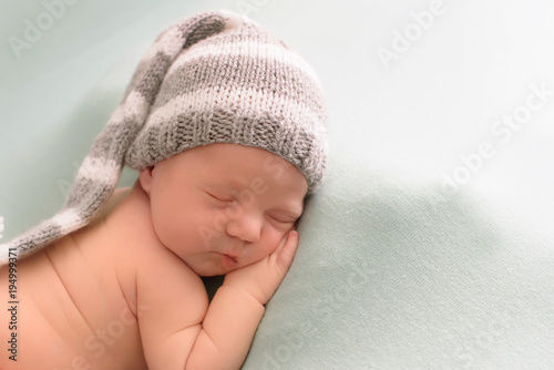 likable and pretty sleeping newborn baby girl with in a knitted hat on a blue background