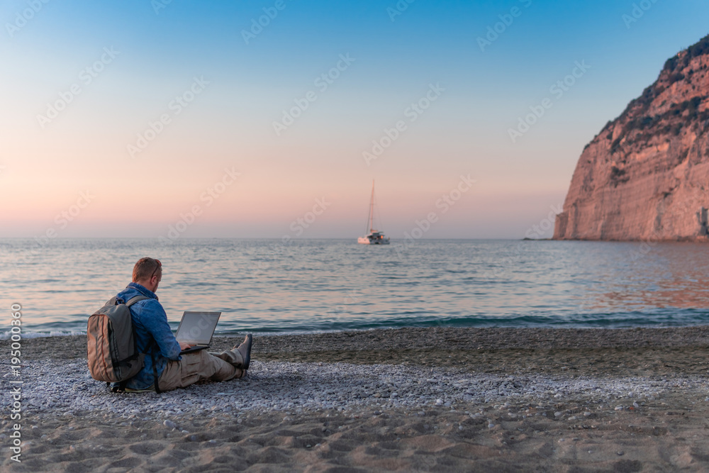 young man with laptop working on the beach. Freedom, remote work, freelancer, technology, internet, travel and vacation concepts