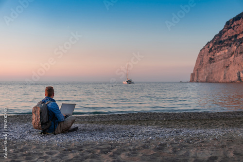 young man with laptop working on the beach. Freedom, remote work, freelancer, technology, internet, travel and vacation concepts