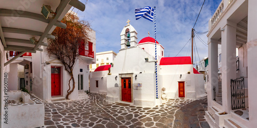 Agia Kyriaki Church, typical Greek church building and Large waving Greek flag against the blue sky on the island Mykonos, The island of the winds, Greece photo