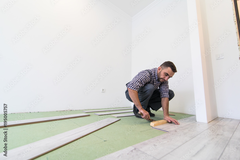 Carpenter worker man installing wood parquet board during flooring work with hammer