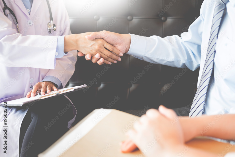 Doctor shakes hands at medical office with patient, wearing glasses, stethoscope and lab coat.