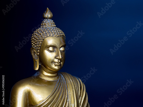Golden antique buddha statue. The background is midnight blue. The face of the Buddha turned to the Left.