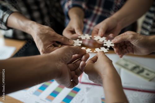 Hands group of business people assembling jigsaw puzzle white. Below is the graph paper business documents placed on a wooden table in the meeting room.