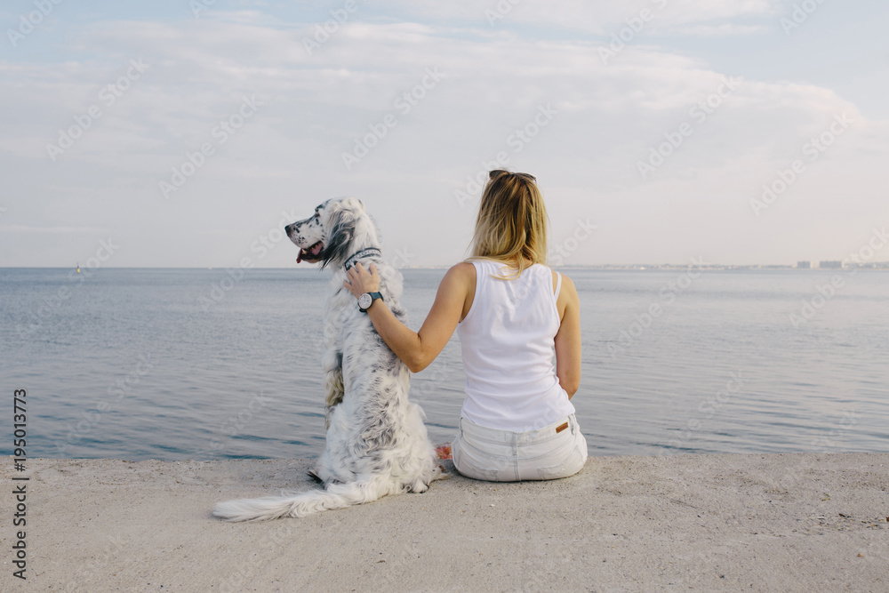 Φωτογραφία young blonde woman with cute white dog sitting in the dock and look at the sea