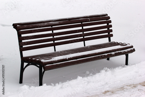 Empty wooden bench in a park covered with snow in wintertime