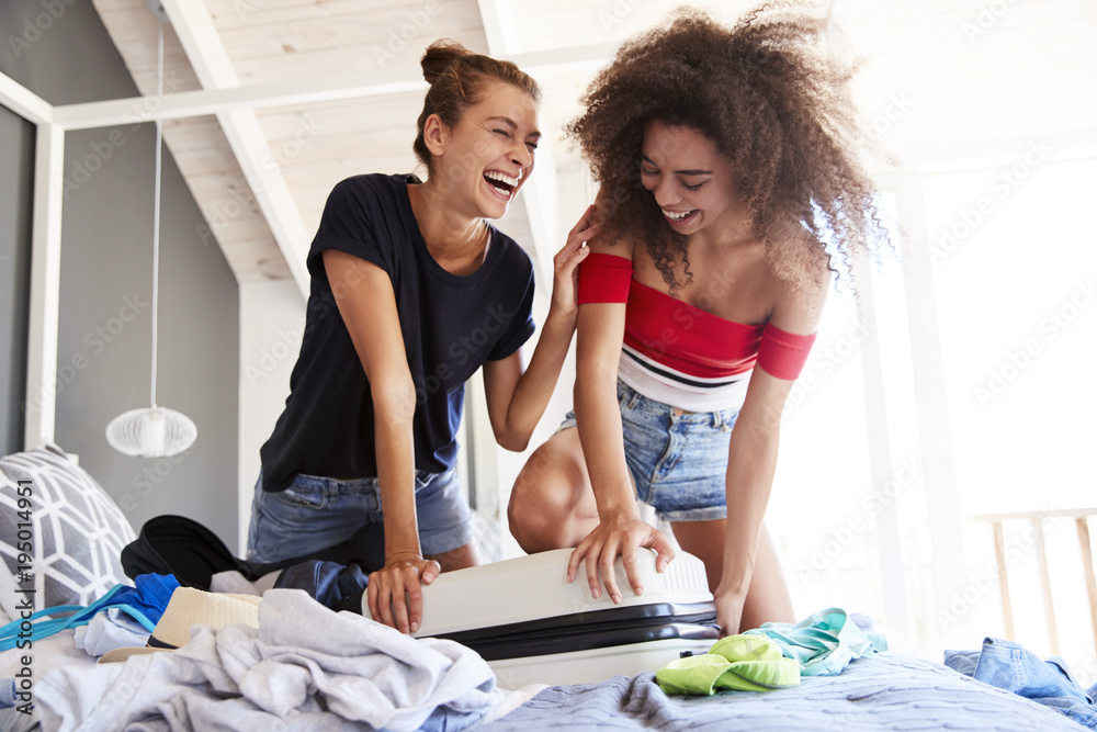 Φωτογραφία Female Friends Trying To Close Full Holiday Suitcase In Bedroom