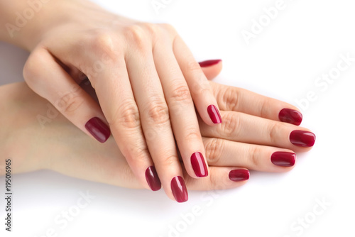 Closeup of hands of a young woman with red manicure on nails against white background