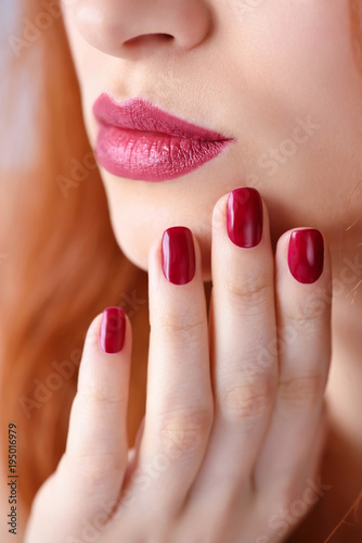 Beautiful red-haired young woman with red manicure  lipstick same color. Close up Portrait.