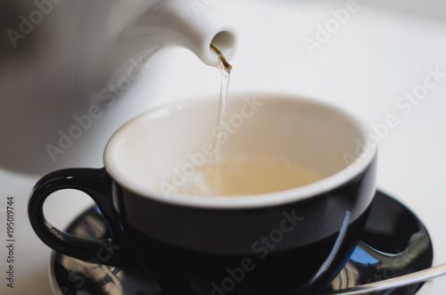 Close up pouring a hot green tea kettle on an oriental style cup on table - natural light