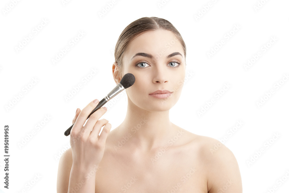 Close-up of a young woman holding brush in her hand and applying makeup. Isolated on light blue background. Close-up of a young woman holding brush in her hand and applying makeup. Isolated on light blue background.