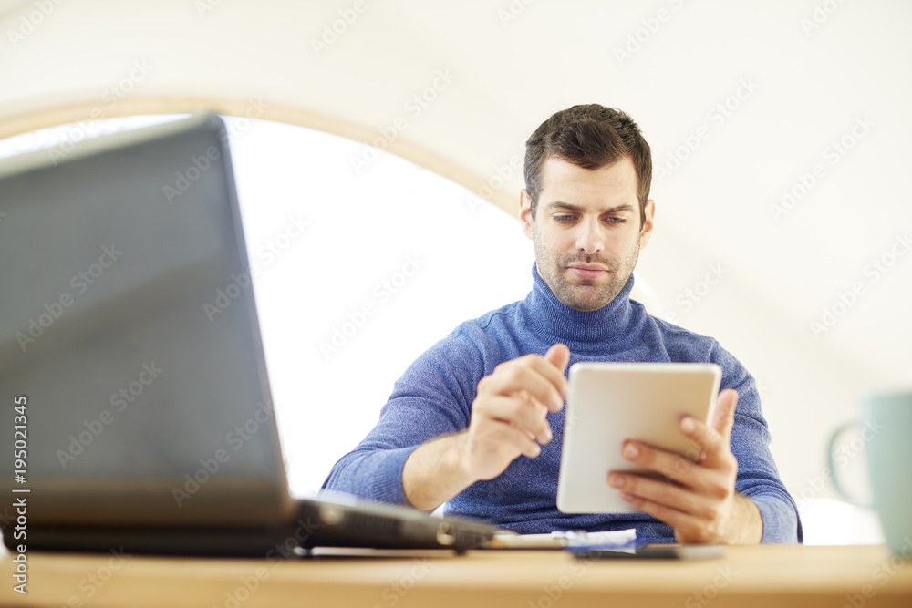 Young man working on digital tablet. Casual young businessman using digital tablet and laptop. Home office. Young man working on digital tablet. Casual young businessman using digital tablet and laptop. Home office.