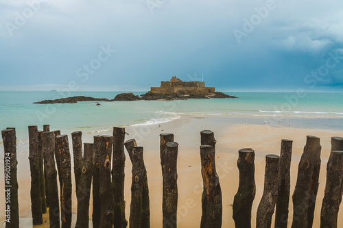 Wooden poles on beach in front of 17-century Fort National on island Petit Be during low tide in Saint-Malo, Brittany, France
