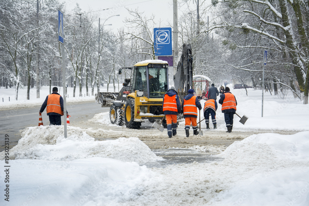 In winter, in snowstorm, workers and a tractor clean the road from snow. In winter, in snowstorm, workers and a tractor clean the road from snow.