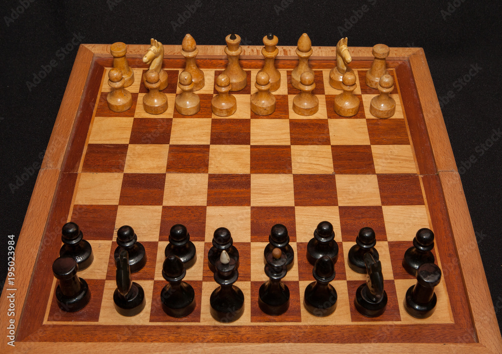 Black and white wooden chess pieces on board with black background Black and white wooden chess pieces on board with black background