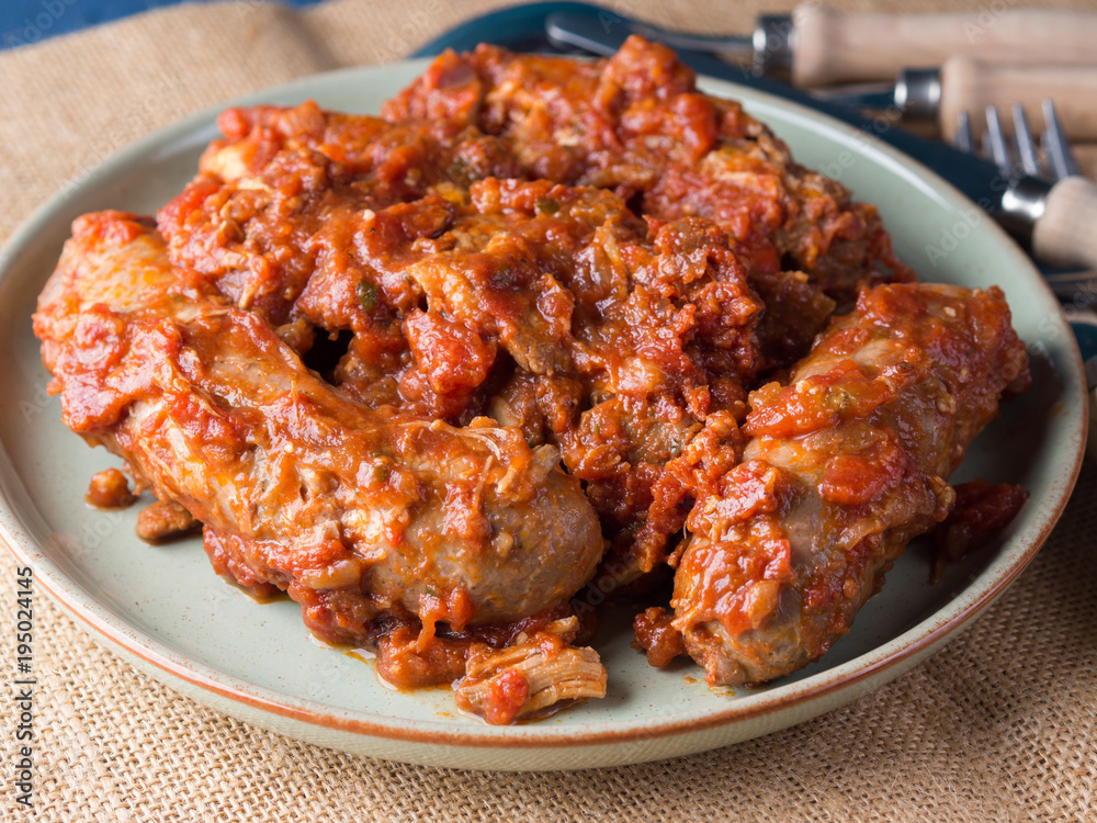 Sausages and pork pullet cooked in traditional Italian tomato ragu sauce. Dish on burlap with cutlery.