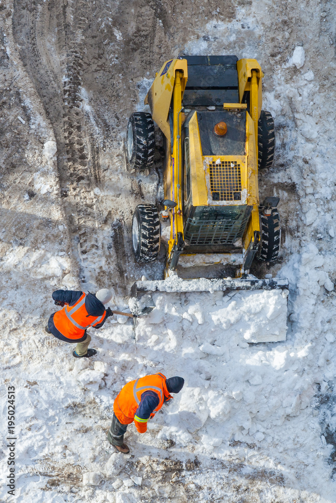 Snow-removing machine and workers in orange uniforms clean the road. Top view