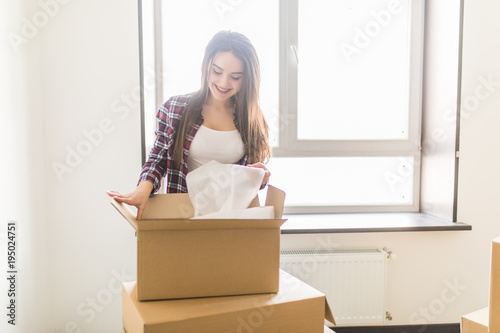 Happy young woman unpacking boxes in new home. Moving comcept photo