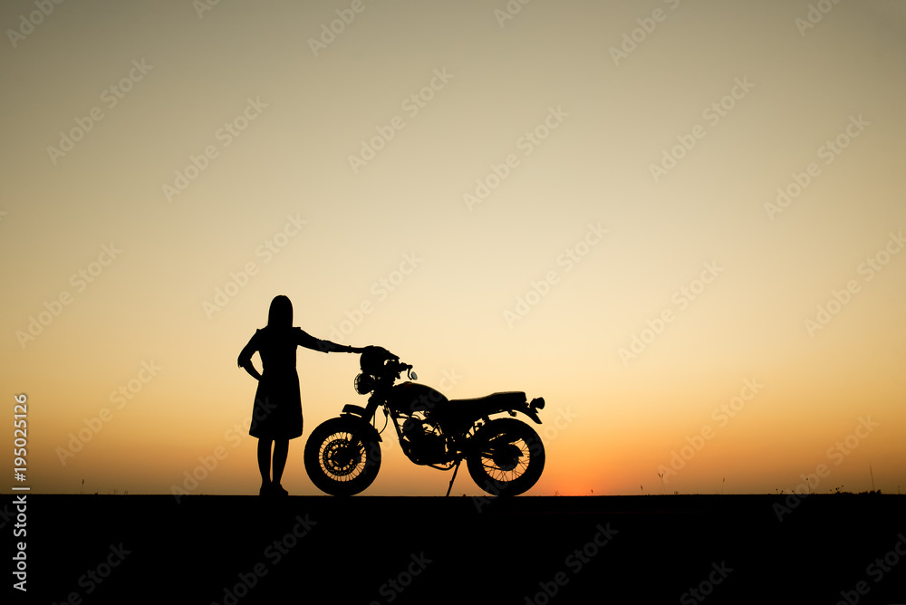 Fototapeta premium Silhouette of beautiful women and motorcycles. She standing with her back,beautiful sunset background,Thailand